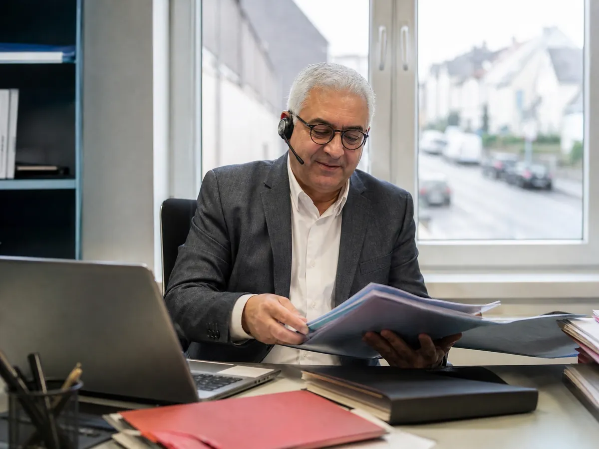 Inhaber einer Agentur für 24-Stunden-Betreuung telefoniert im Büro und sichtet Bewerbungen