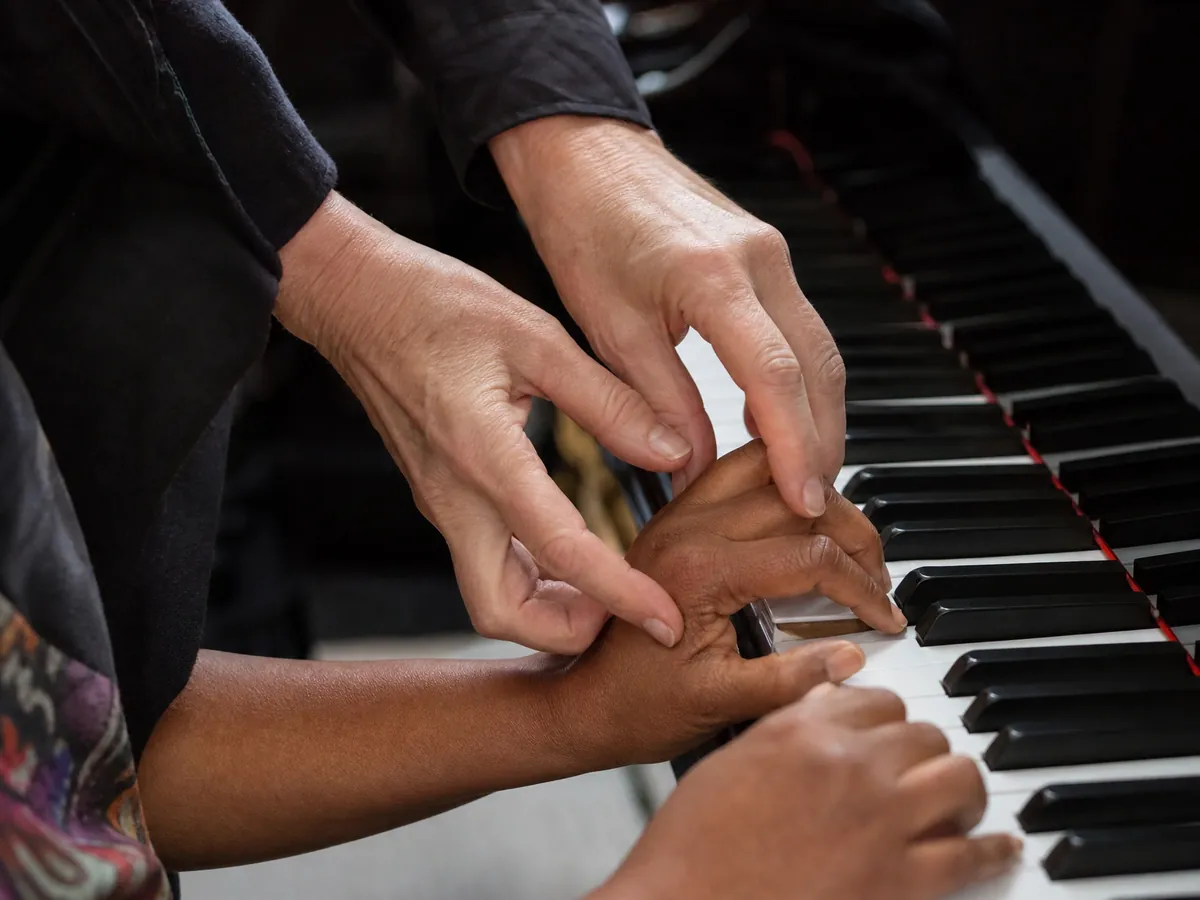 Klavierlehrerin korrigiert die Fingerhaltung einer Schülerin, Musikunterricht ist meist freiberuflich