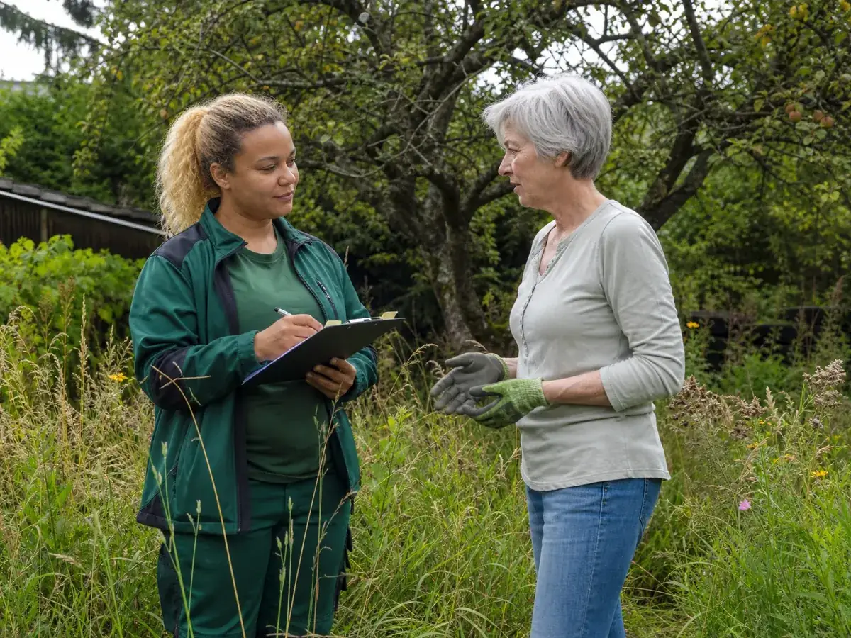 Landschaftsgärtnerin klärt im Garten den Bedarf ihrer Kundin, bevor sie das Angebot schreibt