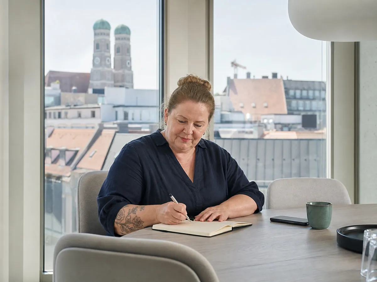 Frau notiert sich mit Blick über München Anlaufstellen für Gründer in ihr Notizbuch