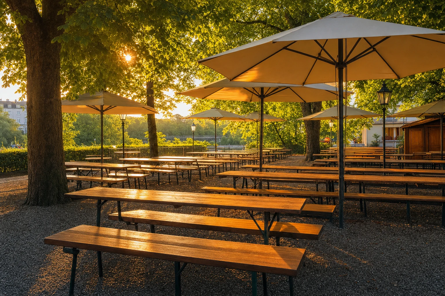 Leerer Biergarten mit langen Holzbänken und aufgespannten Sonnenschirmen unter Bäumen im Abendlicht