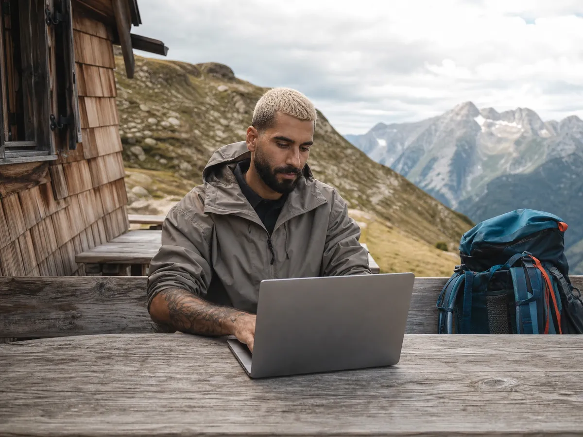 Wanderblogger schreibt vor einer Berghütte, für seinen geschäftsmäßigen Blog braucht er ein Impressum