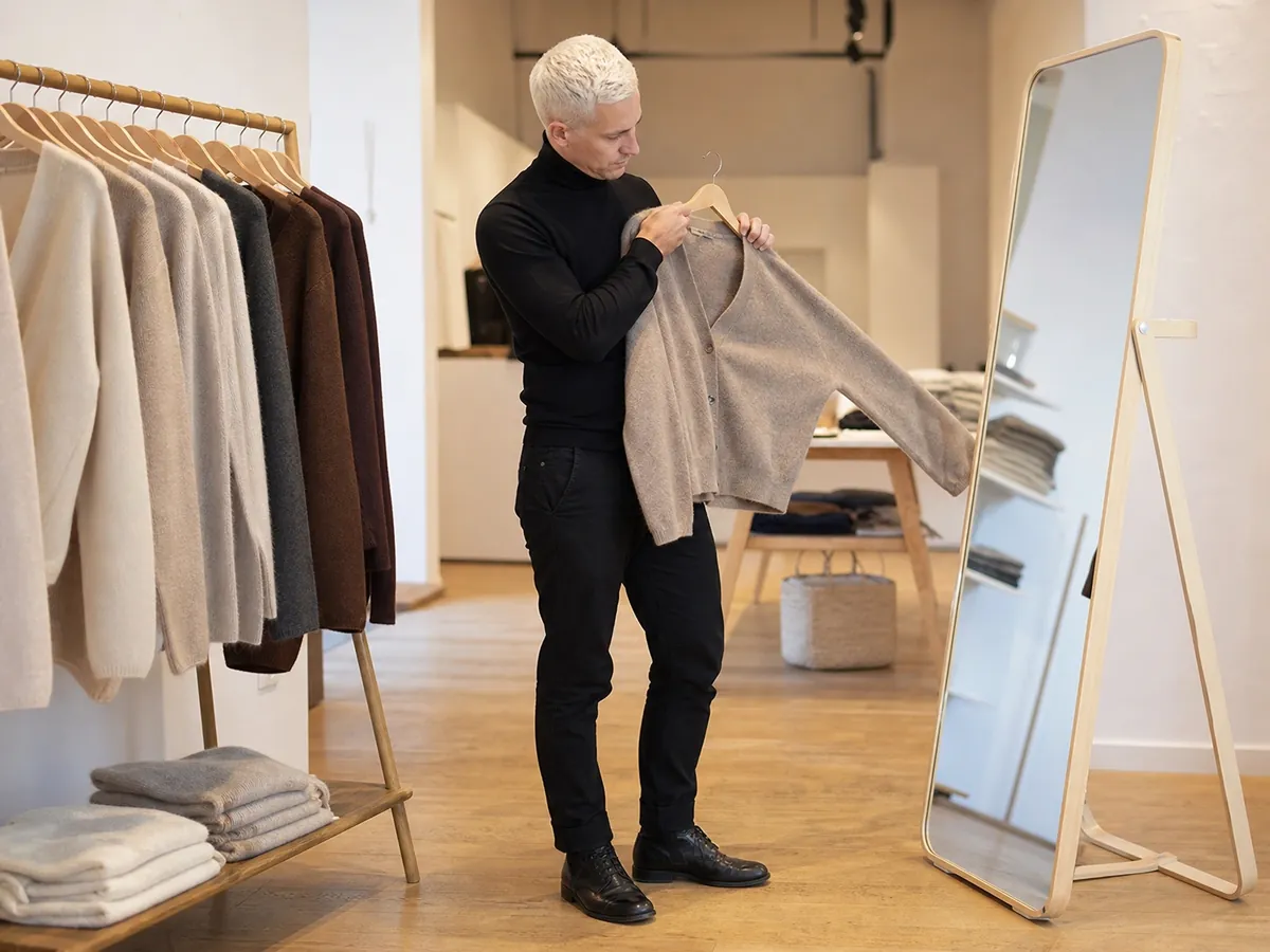 Boutique-Inhaber stellt an der Kleiderstange Strickmode in Naturtönen für sein Sortiment zusammen