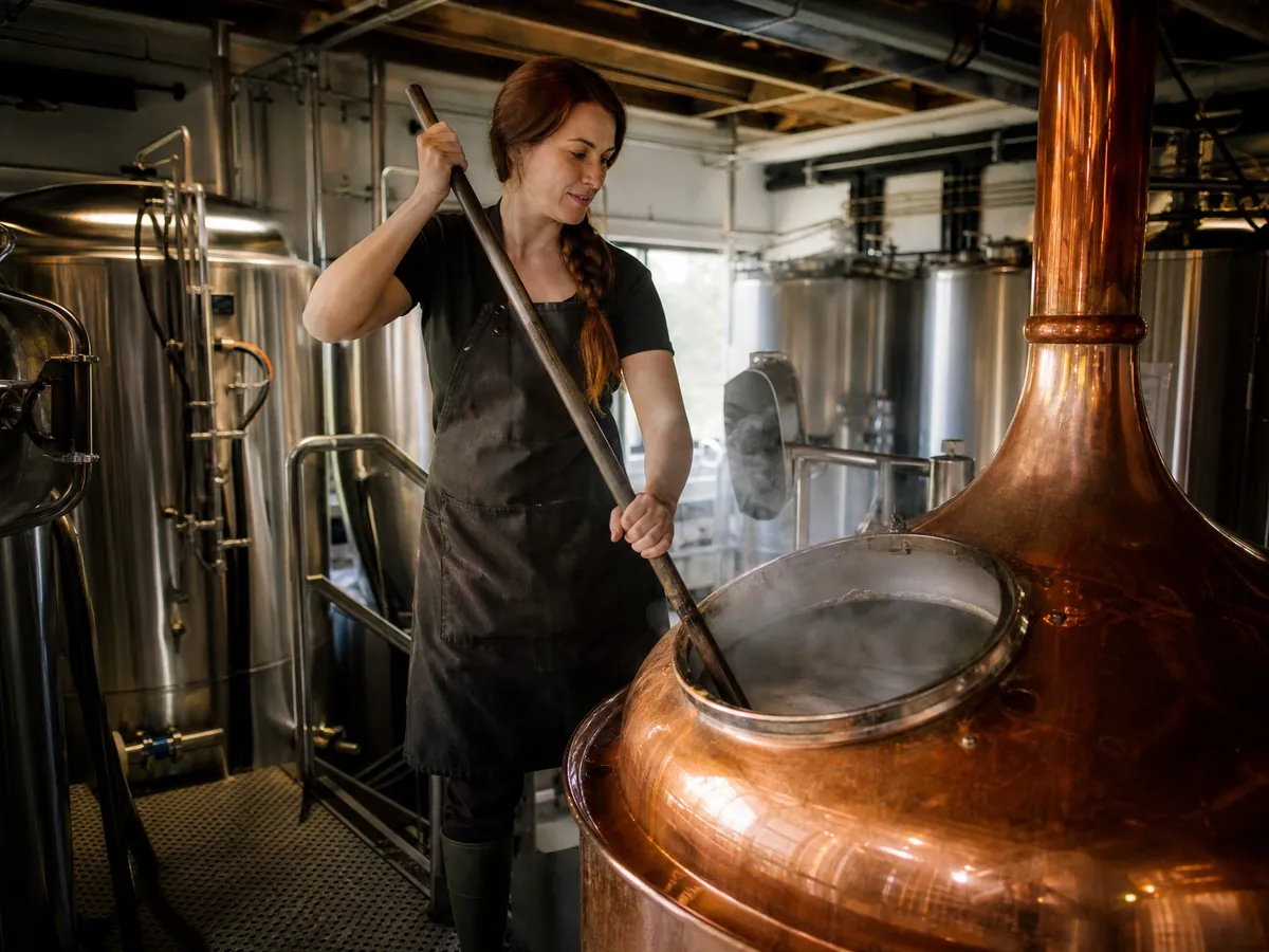Brauerin rührt in ihrer kleinen Brauerei mit dem Maischpaddel im kupfernen Sudkessel