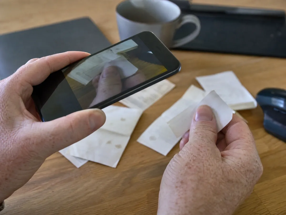 Hand fotografiert einen Kassenbon mit dem Smartphone, um den Beleg digital in der Buchhaltung zu erfassen
