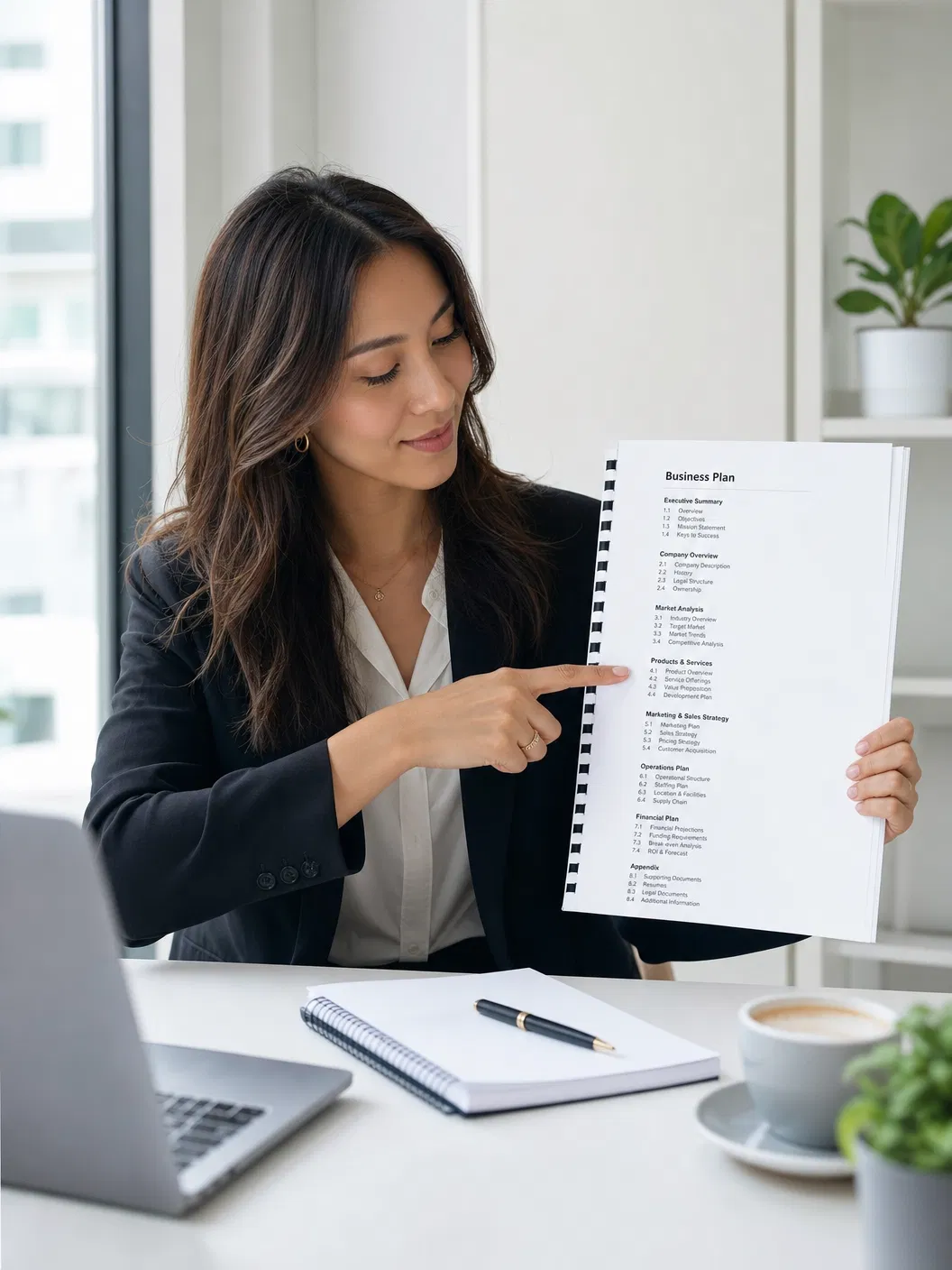 Frau zeigt auf das Inhaltsverzeichnis eines gebundenen Businessplans, auf dem Tisch Laptop, Notizblock und Kaffeetasse