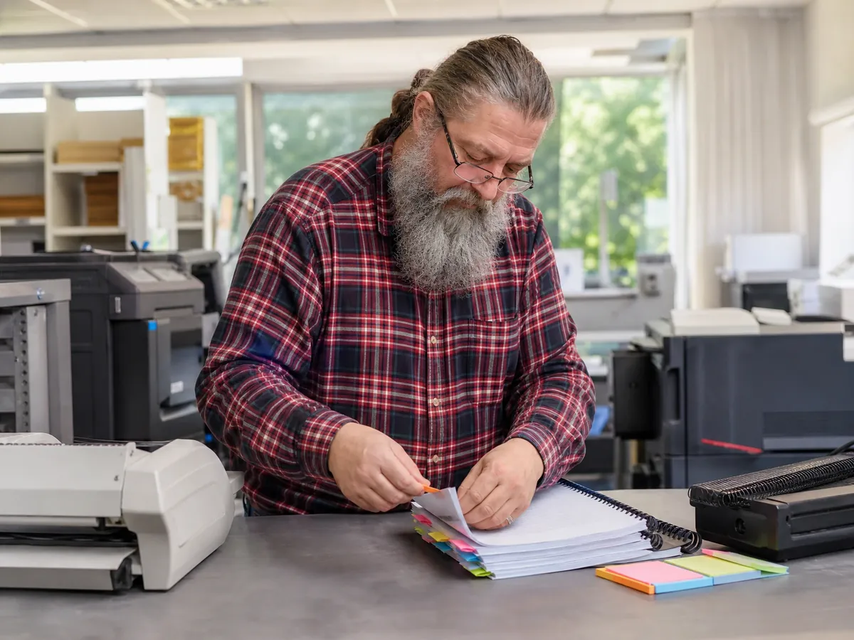 Gründer markiert im Copyshop die Kapitel seines Businessplans mit Registerfähnchen vor dem Binden