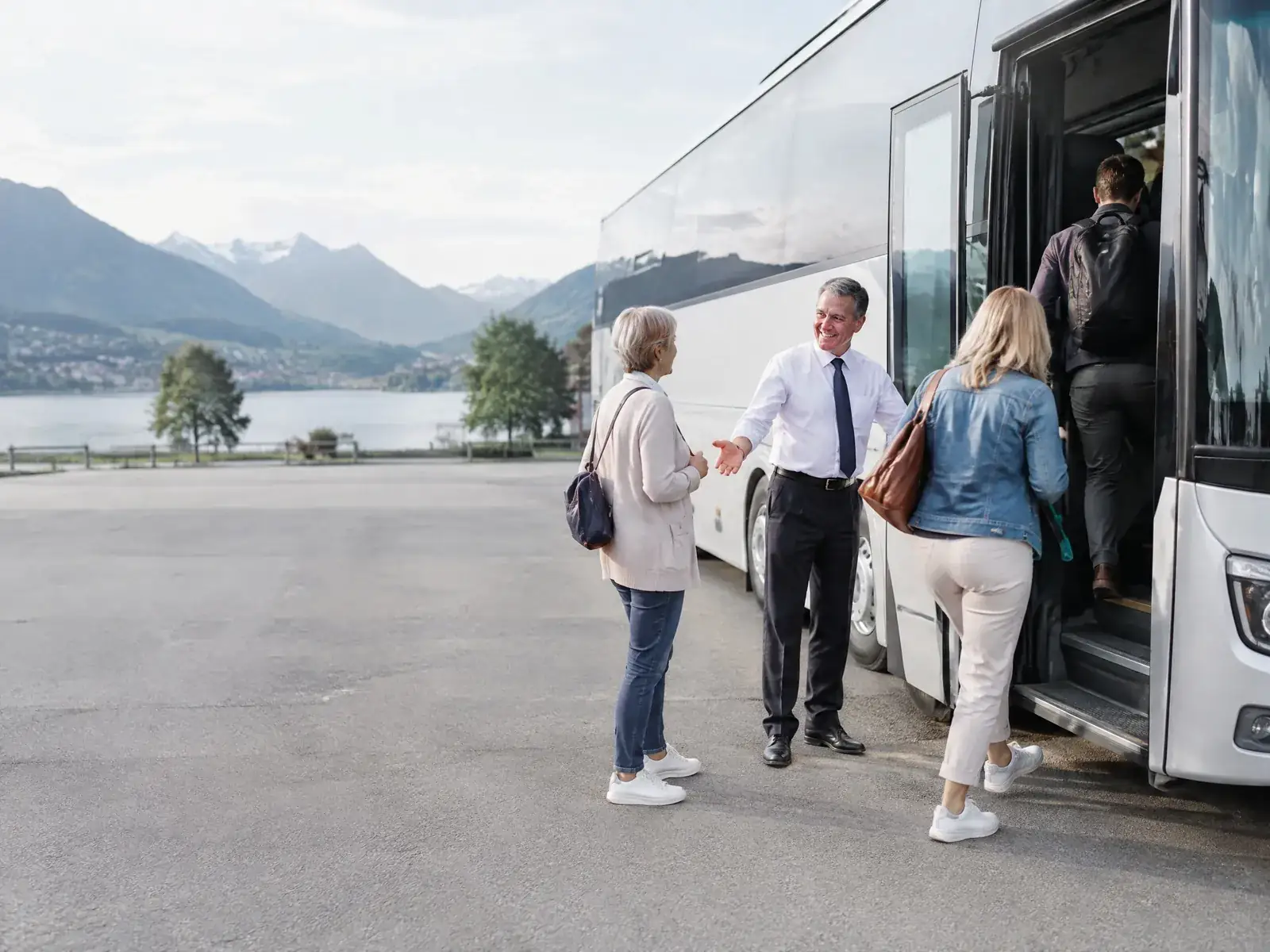 Busfahrer begrüßt eine Reisegruppe beim Einsteigen in einen Reisebus am See