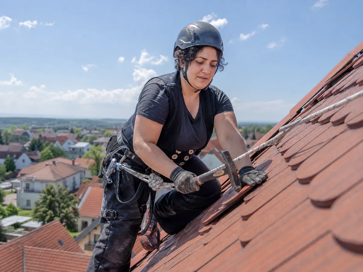 Dachdeckerin deckt mit Sicherungsseil ein Steildach mit Biberschwanzziegeln