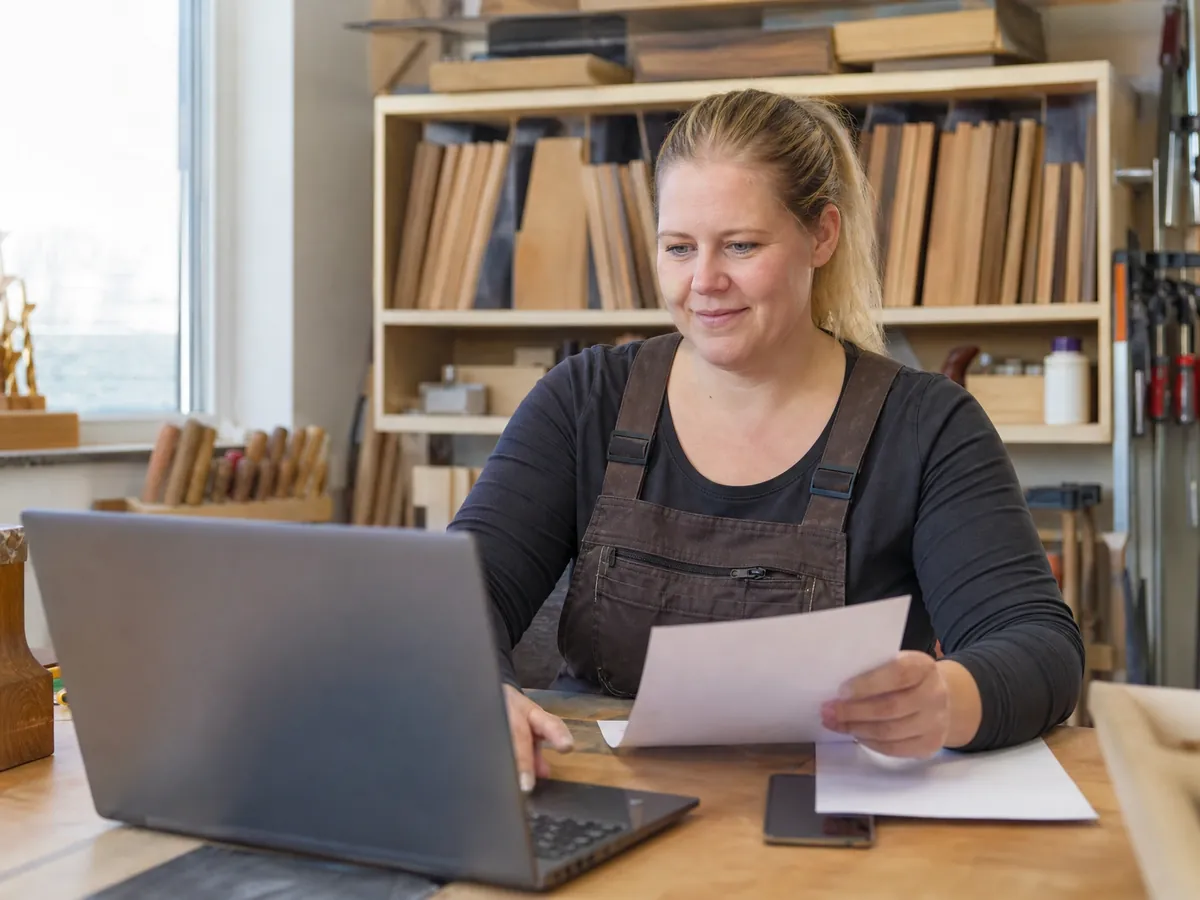 Tischlerin verschickt in ihrem Werkstattbüro eine elektronische Rechnung am Laptop