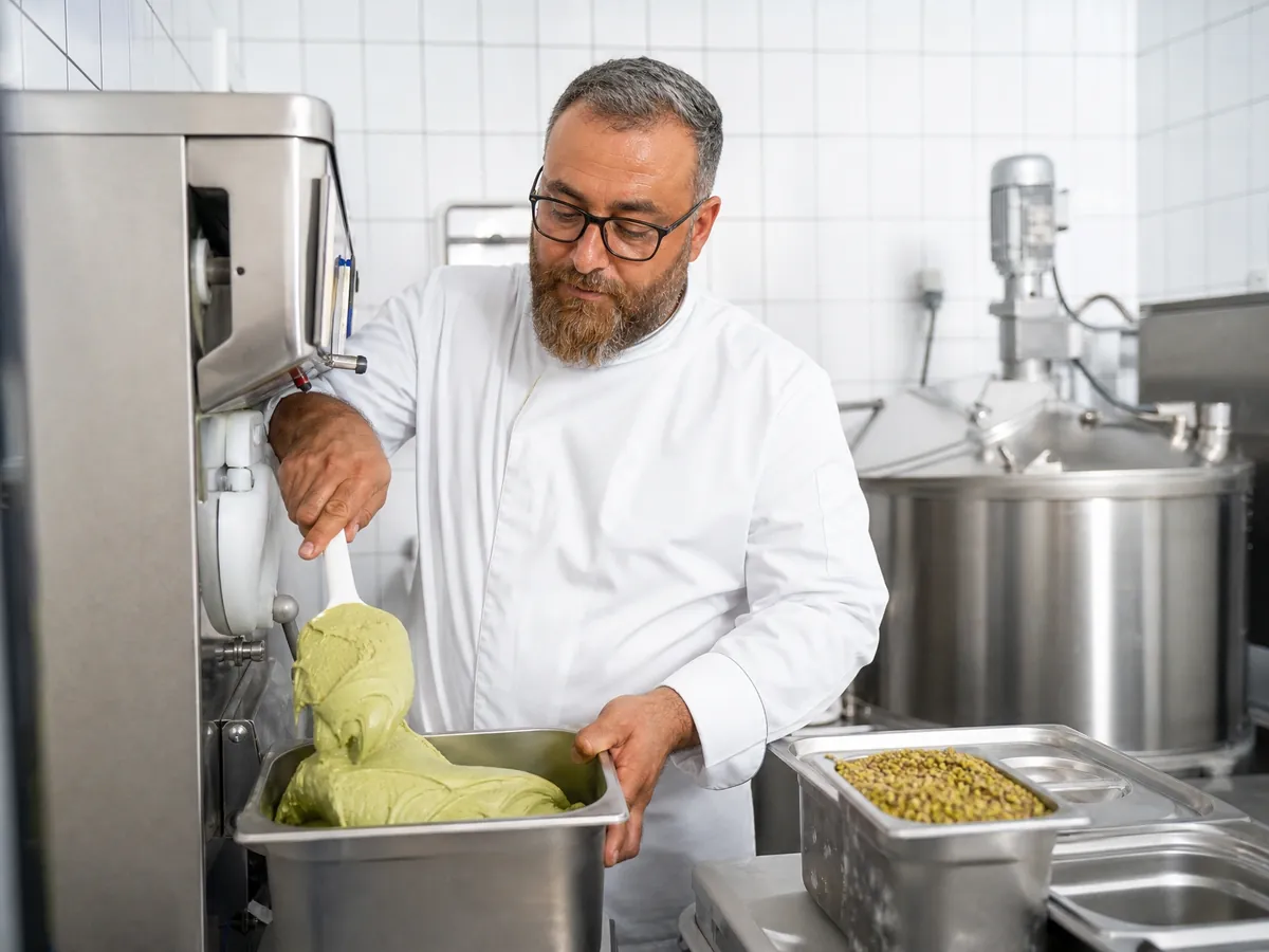 Eismacher zieht im Eislabor seiner Eisdiele frisches Pistazieneis aus der Eismaschine