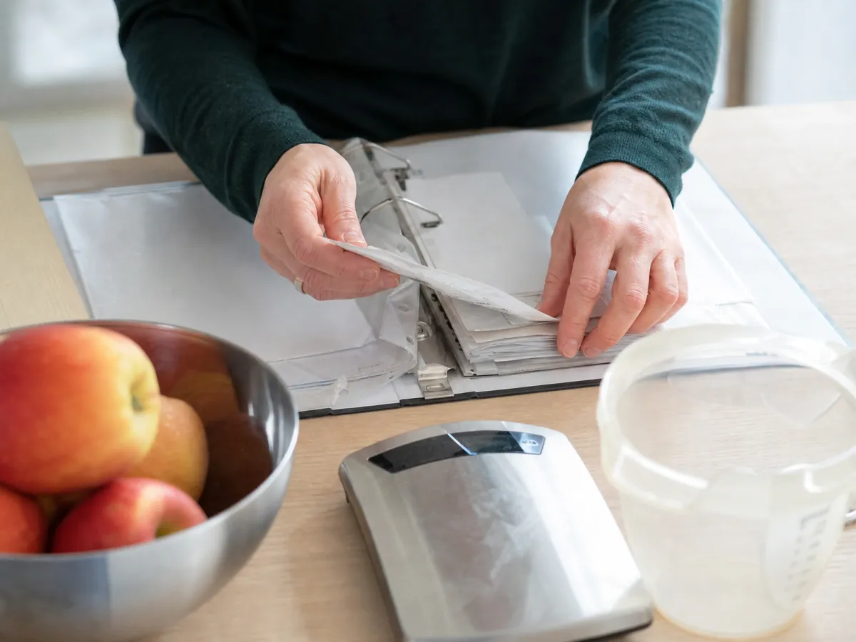 Hände sortieren Quittungen neben Küchenwaage und Messbecher in der Praxis einer Ernährungsberaterin