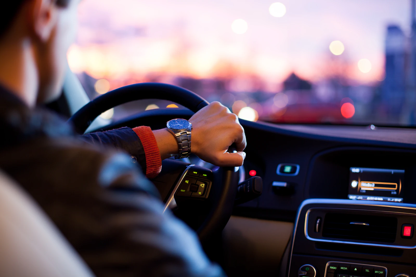 Fahrer hält am Abend das Lenkrad, durch die Frontscheibe leuchten unscharf die Lichter der Stadt
