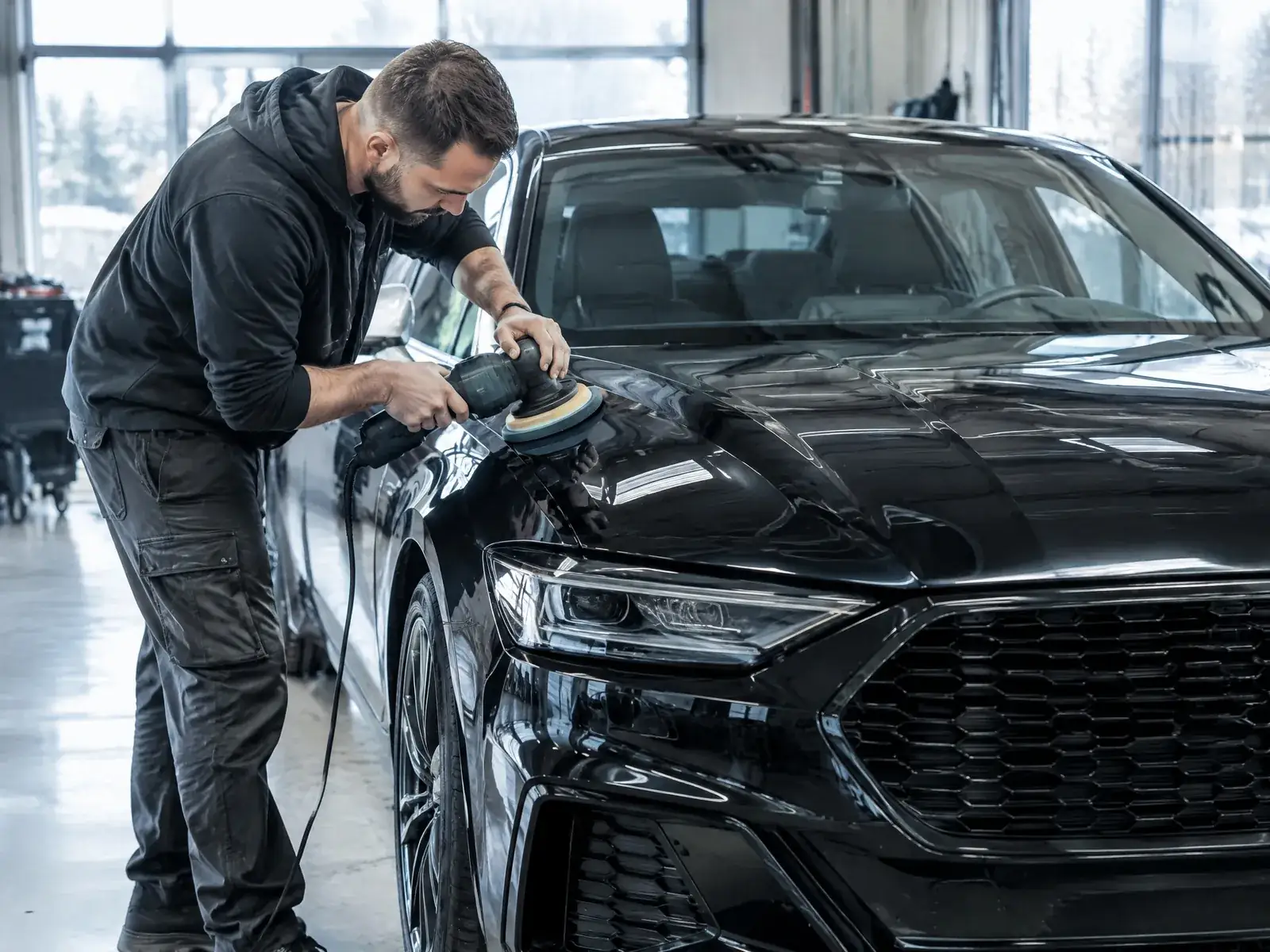 Fahrzeugaufbereitung gründen: Aufbereiter poliert den Lack eines schwarzen Autos