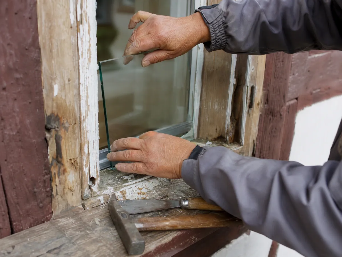 Hände einer Glasermeisterin setzen in Quedlinburg eine Scheibe in einen alten Holzfensterrahmen