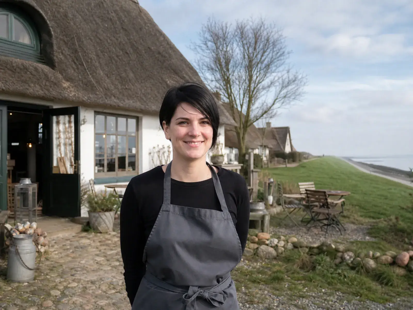 Gründungsförderung in Schleswig-Holstein: Gründerin vor ihrem Café mit Reetdach an der Nordseeküste