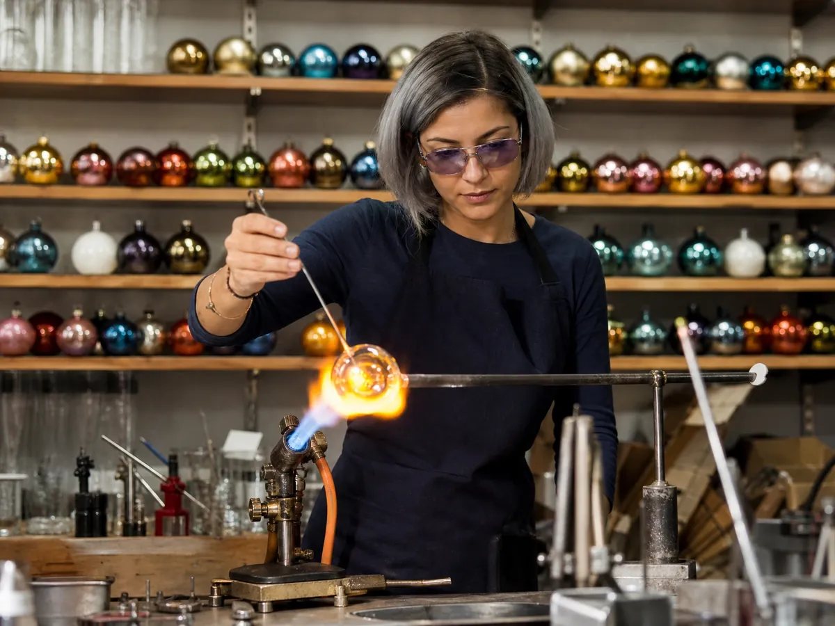 Junge Glasbläsermeisterin formt in ihrer Werkstatt in Lauscha eine Christbaumkugel