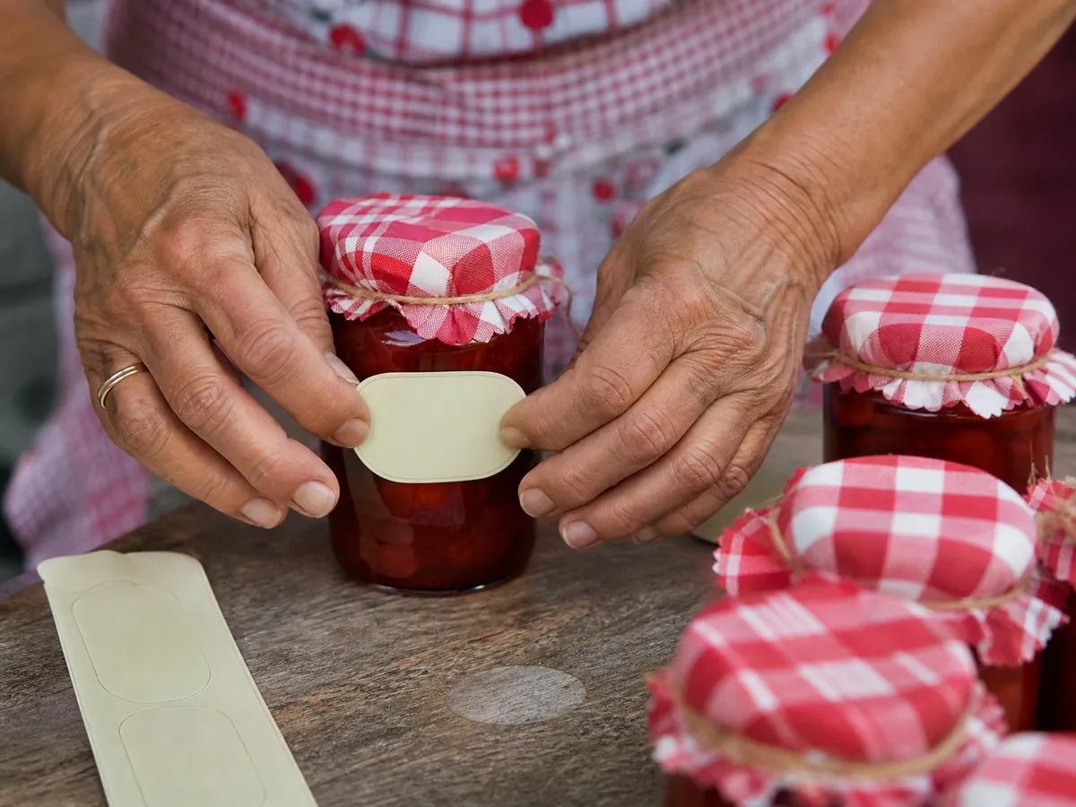 Hände bekleben im Hofladen ein Glas selbst gemachte Marmelade mit einem Etikett