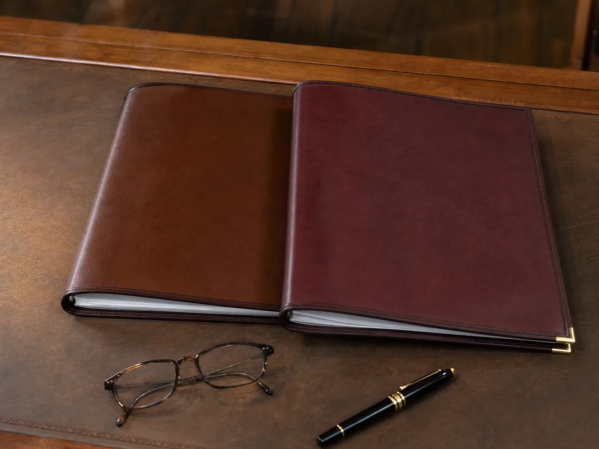 Zwei Ledermappen, eine Brille und ein Füller auf einem Schreibtisch