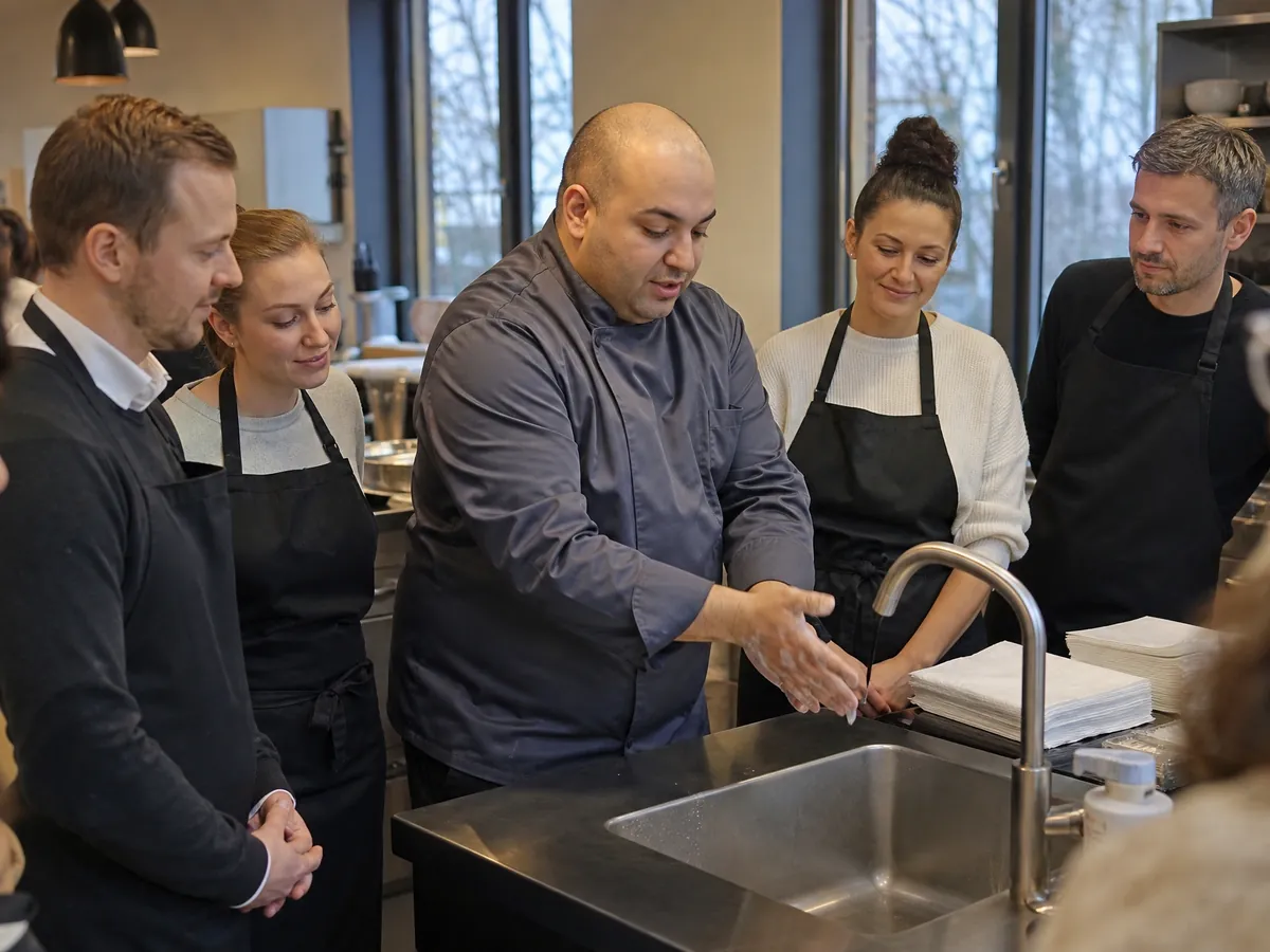 Leiter einer Kochschule weist die Teilnehmenden vor dem Kurs in die Händehygiene ein