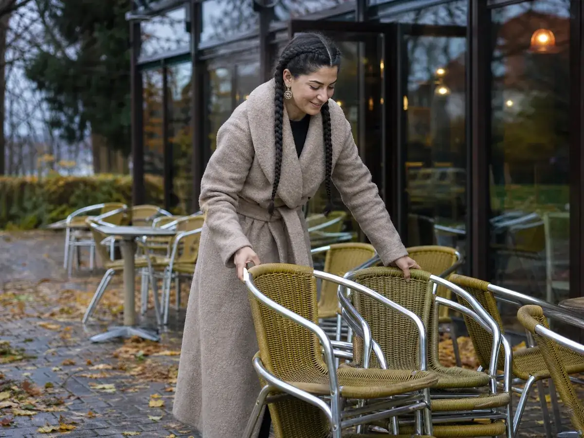 Betreiberin eines Eiscafés räumt im Herbst die Terrasse, wenn der Umsatz saisonal sinkt