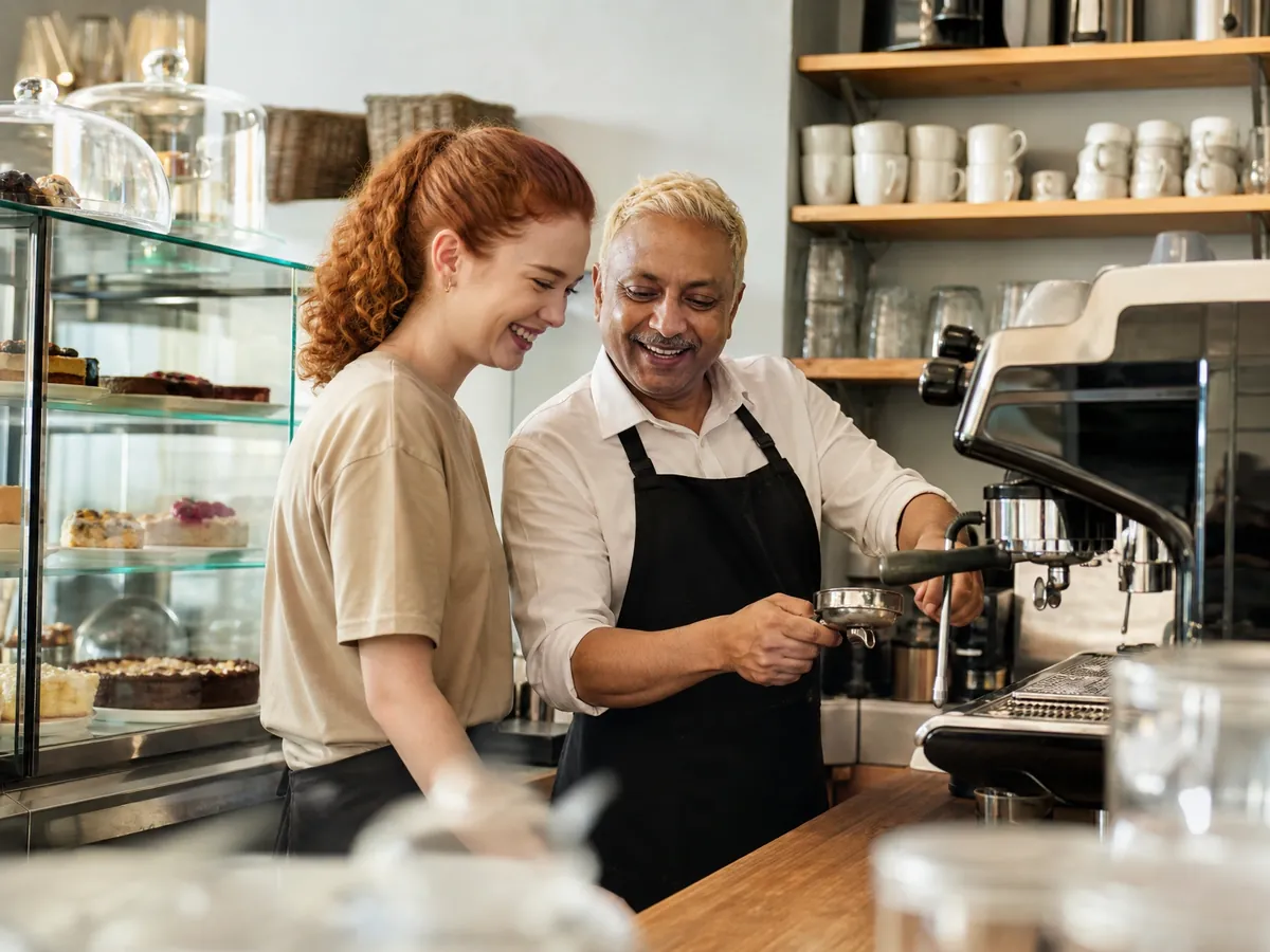 Café-Inhaber arbeitet eine neue Minijobberin an der Siebträgermaschine hinter dem Tresen ein