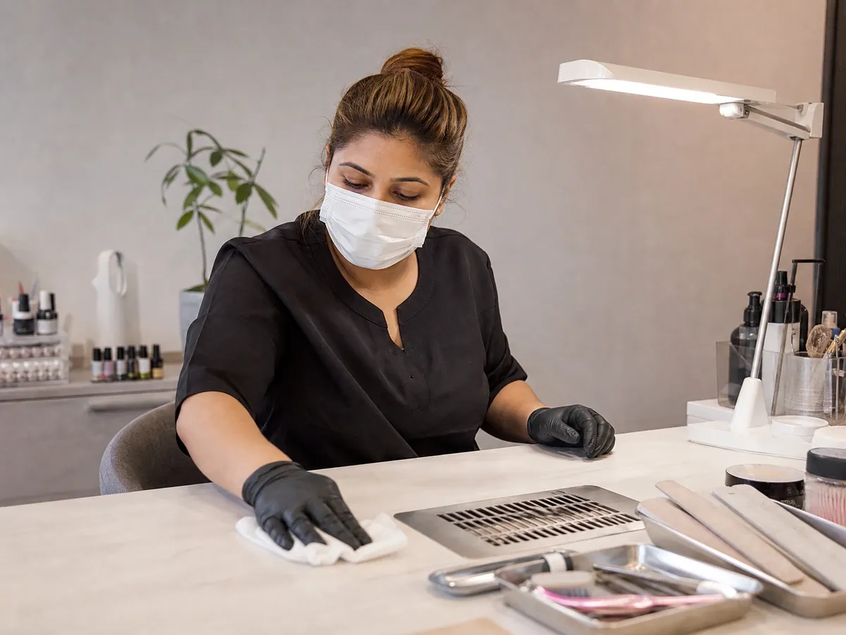 Nageldesignerin desinfiziert in ihrem Nagelstudio Arbeitstisch und Instrumente vor der Kundin