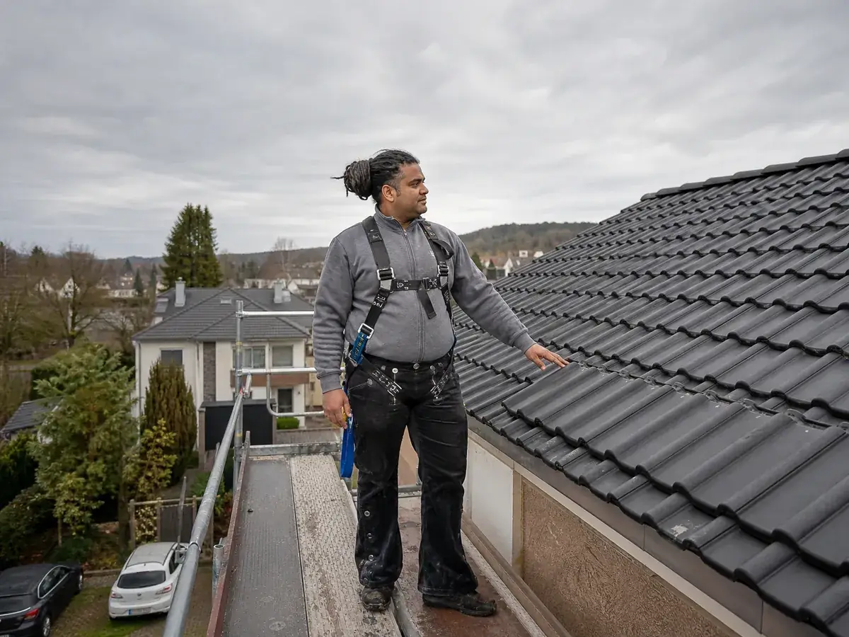 Dachdecker prüft auf dem Gerüst ein neu gedecktes Dach, ein Beruf mit hohem Haftungsrisiko