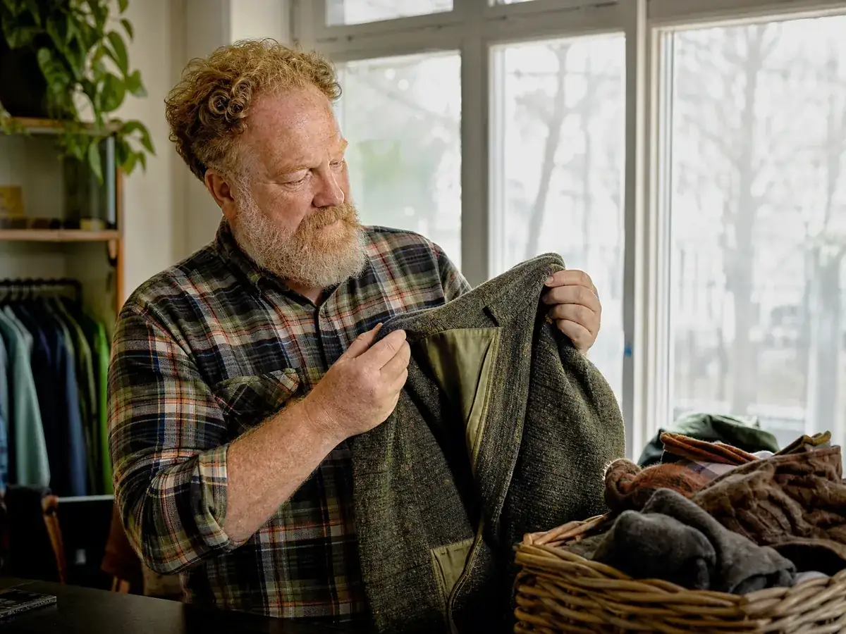 Inhaber eines Second-Hand-Ladens prüft bei der Warenannahme eine Wolljacke auf Löcher