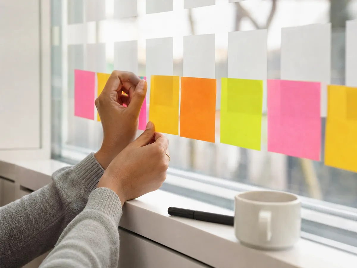Hände ordnen Haftnotizen als Zeitleiste für die Gründung aus der Arbeitslosigkeit Schritt für Schritt