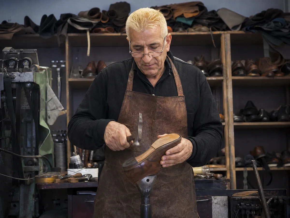 Selbstständiger Schuhmacher besohlt einen Lederschuh, Thema Krankenversicherung bei Minijob