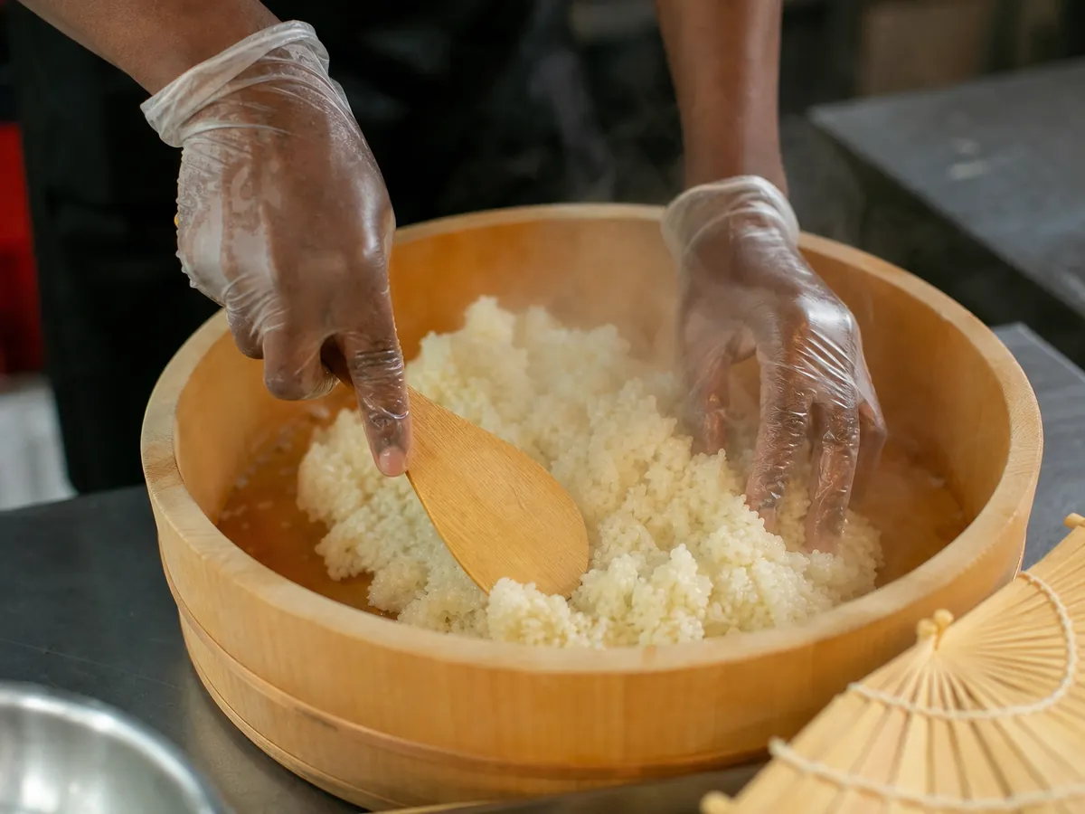 Hände wenden gesäuerten Sushi-Reis in einer Holzschüssel, damit er nach dem Kochen zügig abkühlt