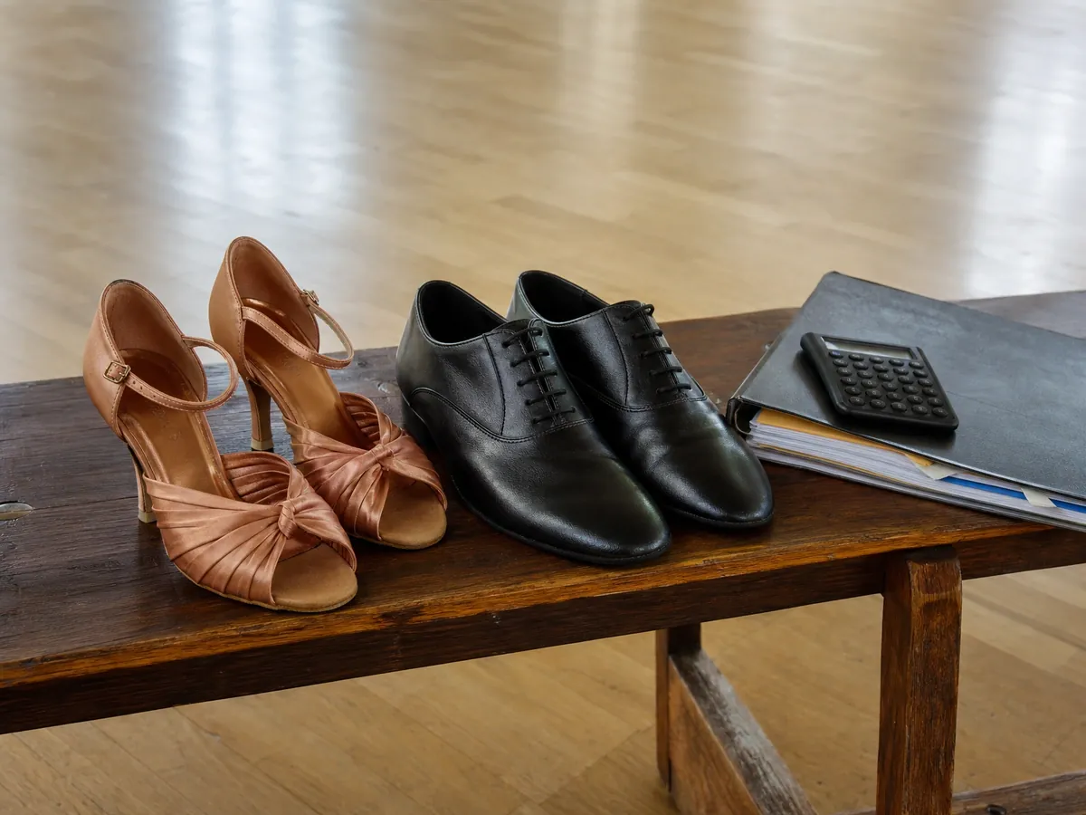 Tanzschuhe am Rand des Parketts neben Ordner und Taschenrechner für die Umsatzsteuer der Tanzschule