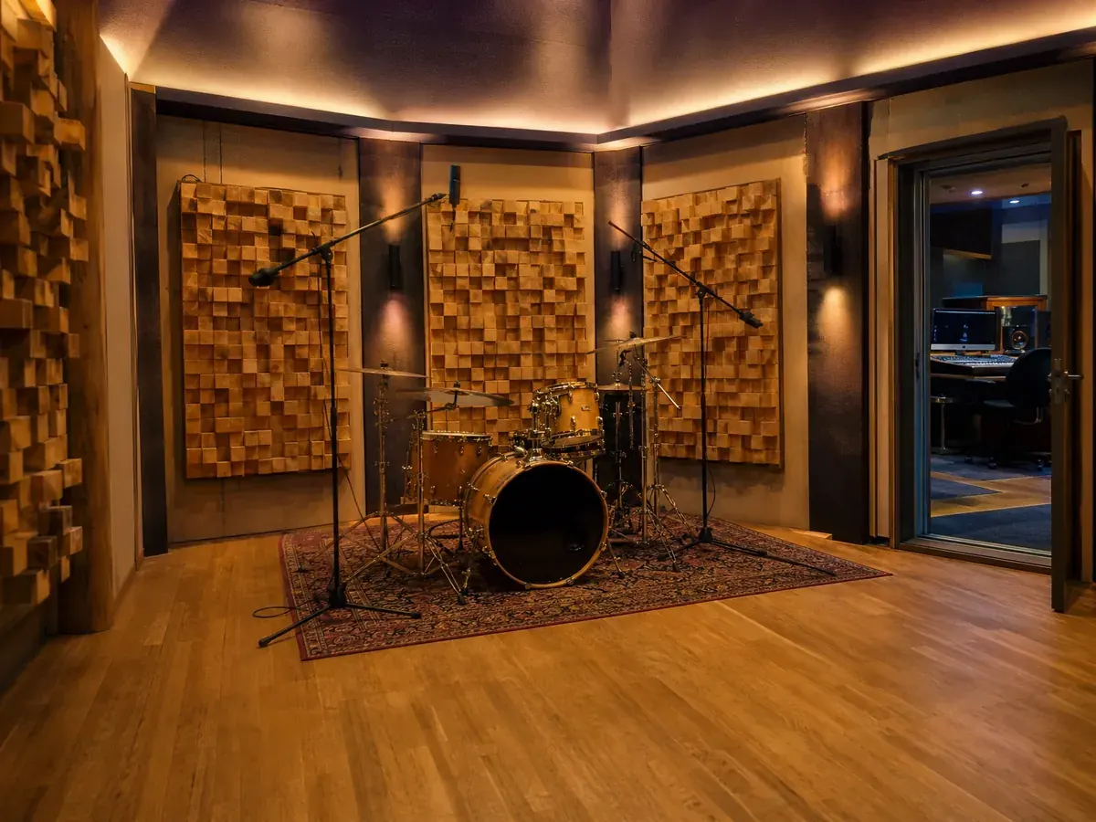 Aufnahmeraum eines Tonstudios mit Schlagzeug, Mikrofonen und Holzdiffusoren, einem großen Kostenblock