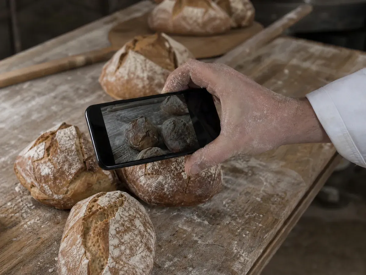 Bäcker fotografiert frisch gebackene Brote mit dem Smartphone für Beiträge zur Kundengewinnung