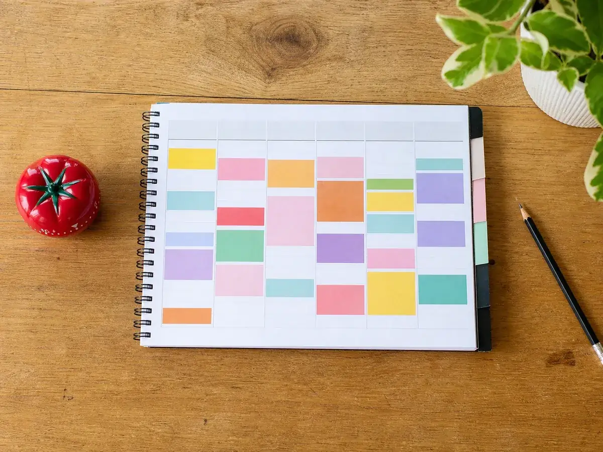 Wochenplaner mit Farbblöcken und Tomaten-Küchentimer für feste Arbeitsintervalle im Zeitmanagement